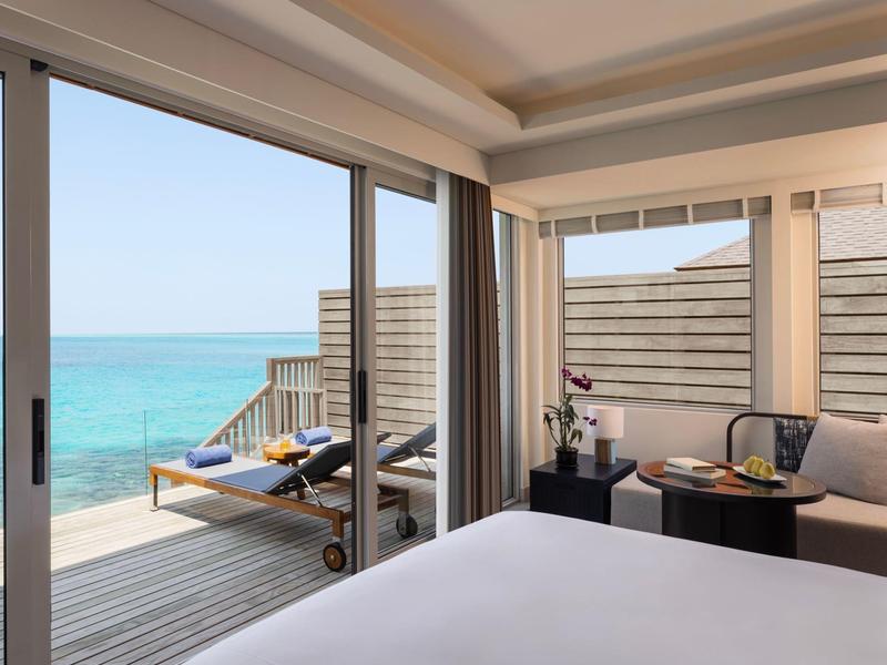 View from hotel room with bed to terrace and sea on clear day.