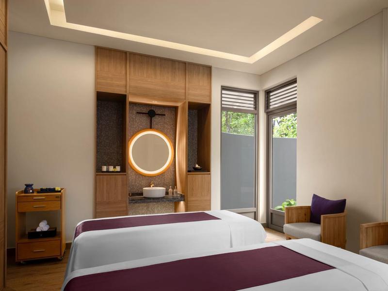 Modern hotel room with two beds, wood paneling, and natural light from windows.