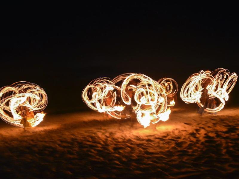 Fire twirlers create light patterns at night on sand.