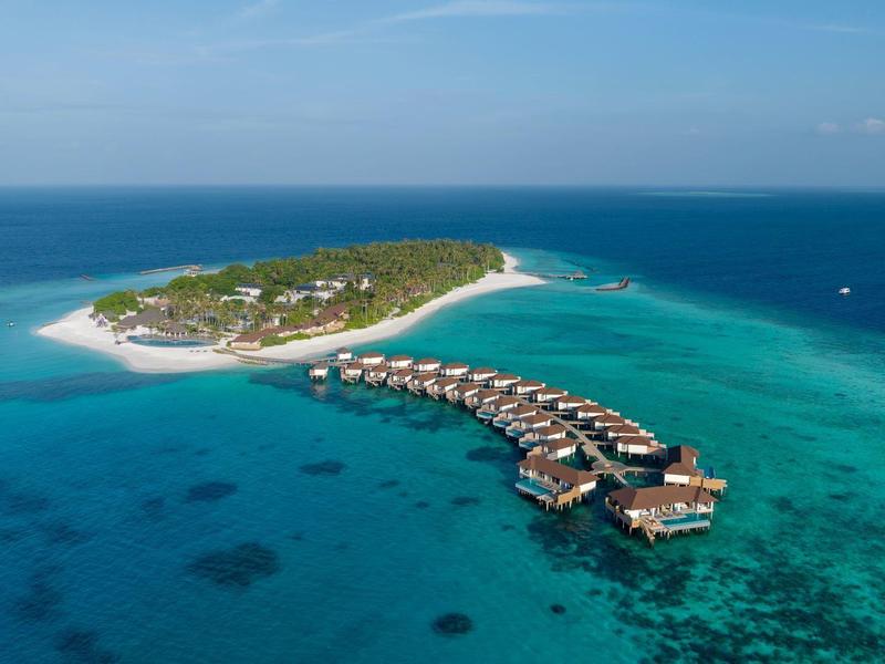 Island with overwater bungalows surrounded by clear blue sea.