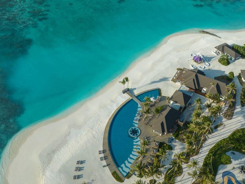 Aerial view of a resort with pool on white sandy beach and turquoise sea.