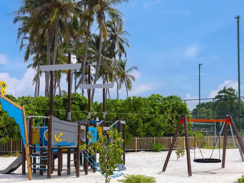 Children's playground with climbing frame, slides and swings in front of palm trees and blue sky