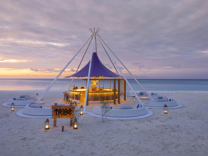 A tent restaurant on the beach with sunbeds and a bar at sunset.