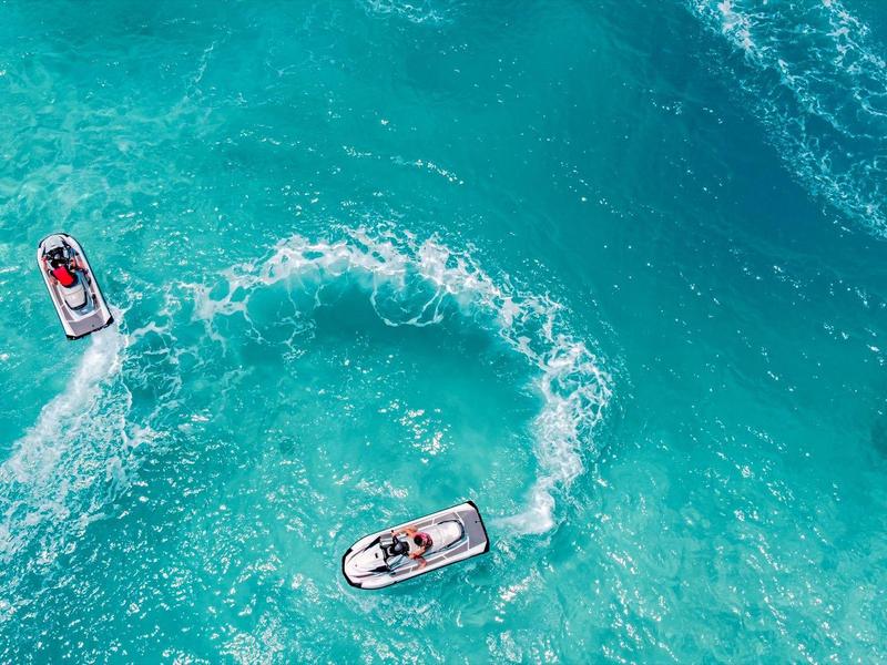 Three jet skis move on turquoise water, leaving swirling trails behind.
