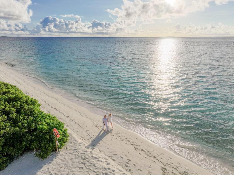 Pár prochází tichou písčitou pláží s čistou vodou a slunečnou oblohou.