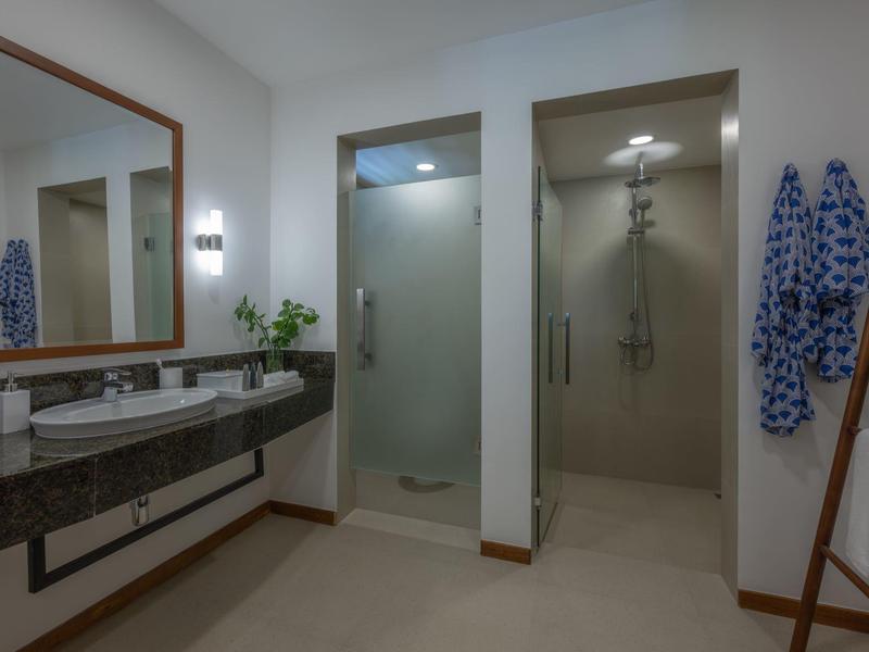 Moderní hotelová koupelna s dvojitým umyvadlem, sprchovým koutem a ručníky na zdi.