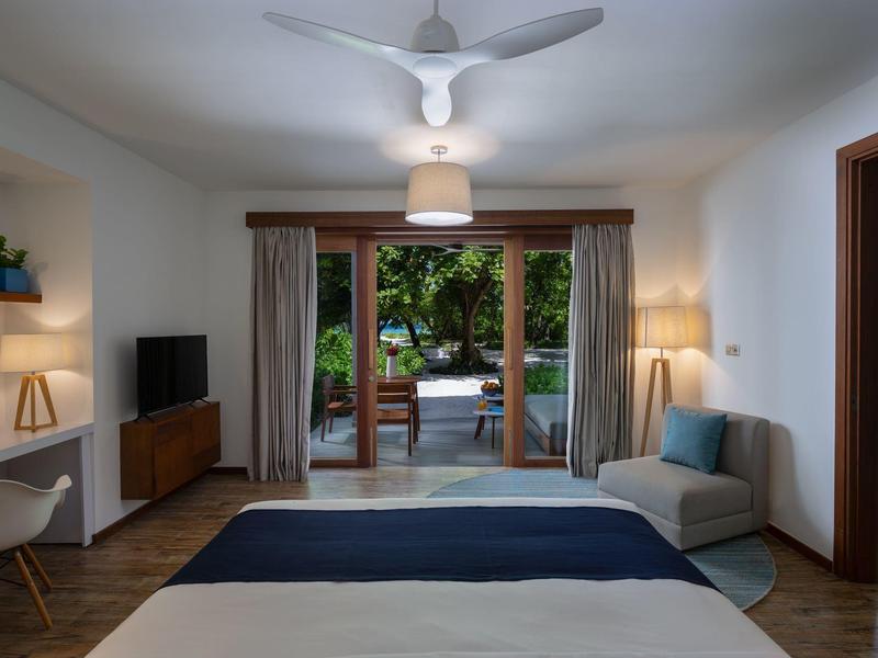 Moderní hotelový pokoj s manželskou postelí, lounge koutkem a výhledem na terasu s bazénem.