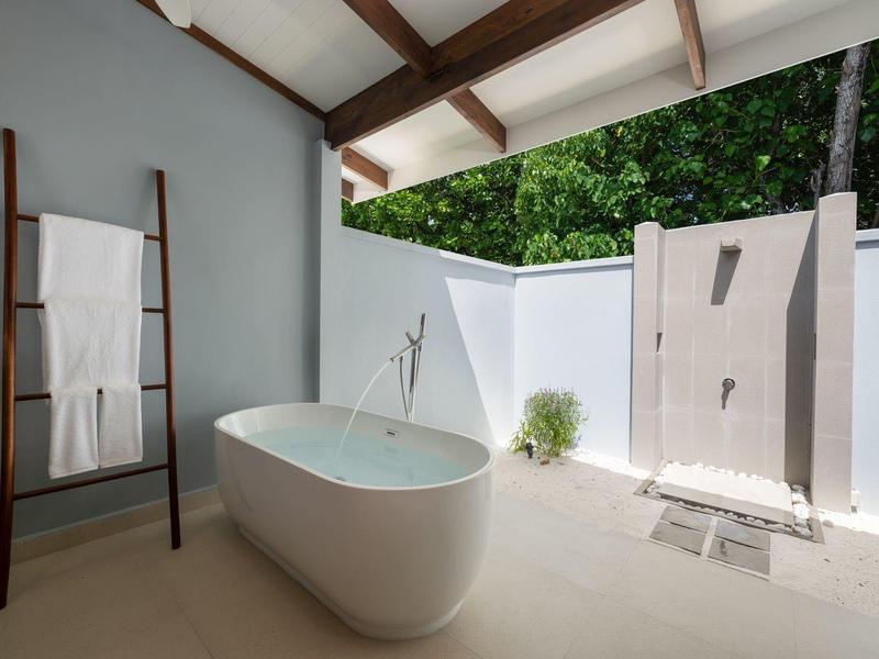 Moderní koupelna s volně stojící vanou a venkovní sprchou za bílou zdí.