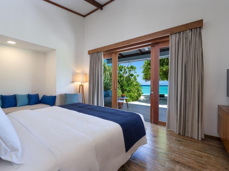 Moderní hotelový pokoj s velkou postelí a výhledem na bazén přes skleněné posuvné dveře.