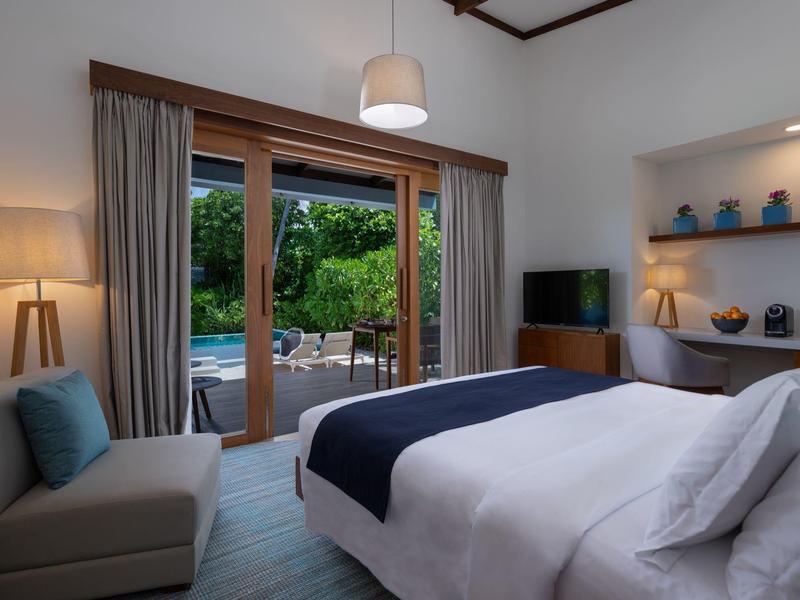 Pohodlný hotelový pokoj s výhledem na bazén a zahradu skrz velké posuvné dveře.
