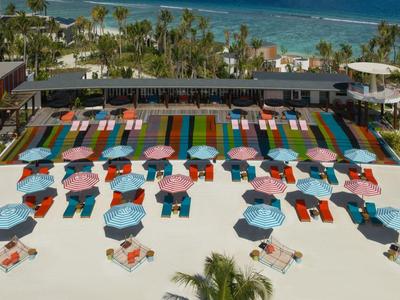 Plage avec chaises longues colorées et parasols devant une station balnéaire avec piscine et palmiers au bord de la mer