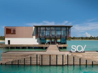Maison de plage moderne sur une jetée avec façade en verre donnant sur la mer sous un ciel clair.