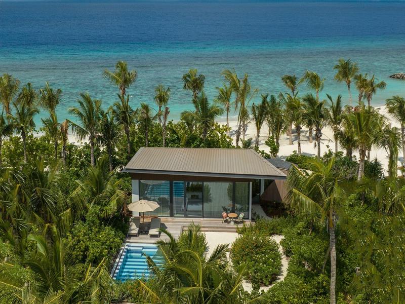 Moderne villa met zwembad tussen palmbomen op wit zandstrand met blauwe zee op de achtergrond.
