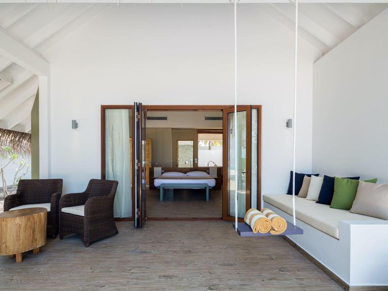 Camera d'hotel moderna e luminosa con letto a dondolo, divano e vista su un'altra stanza con letto.