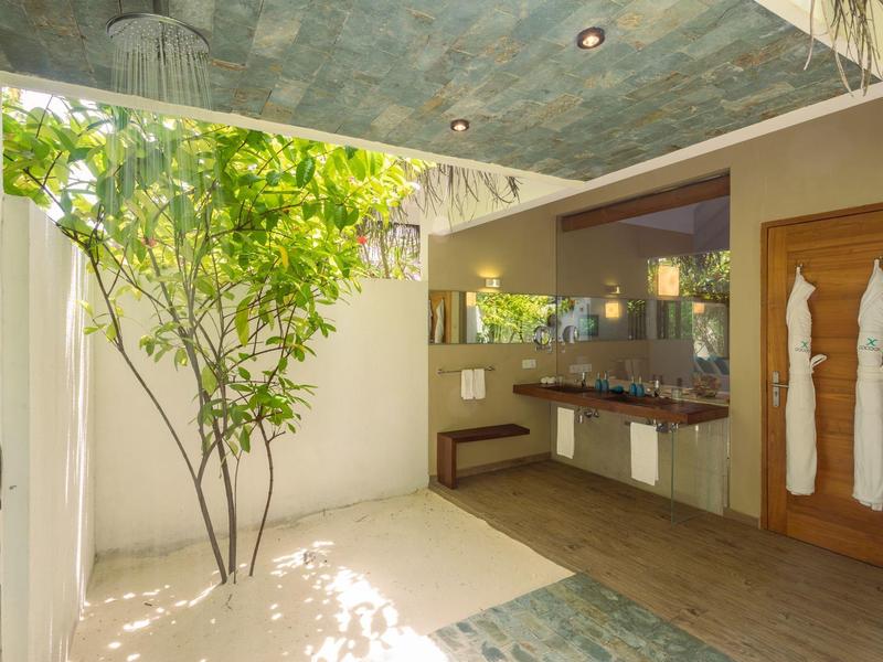 Bagno aperto con albero verde, pavimenti in legno e due accappatoi bianchi appesi al muro.