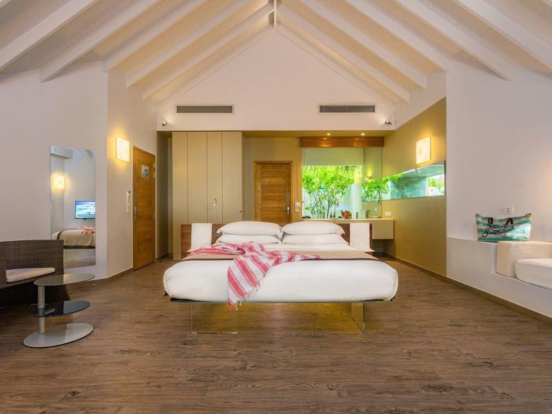 Camera d'hotel moderna con letto matrimoniale, pavimento in legno e grande finestra con vista sul verde.