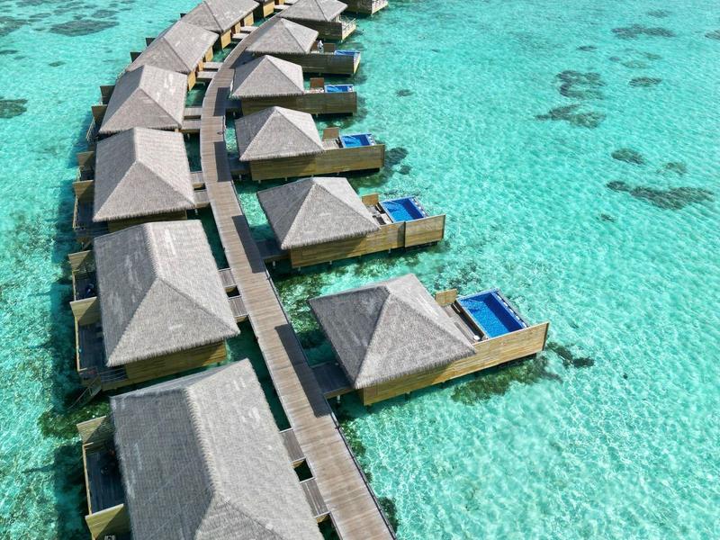 Bungalow su acqua turchese chiara collegati da passerelle a semicerchio.