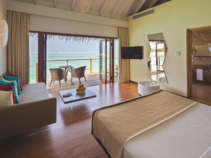 Camera d'hotel moderna con vista mare, balcone con sedie e tavolo, arredi accoglienti.