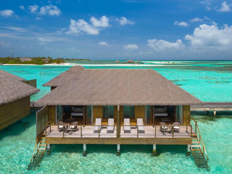 Bungalow su palafitte sopra acqua turchese limpida con ombrelloni e lettini.