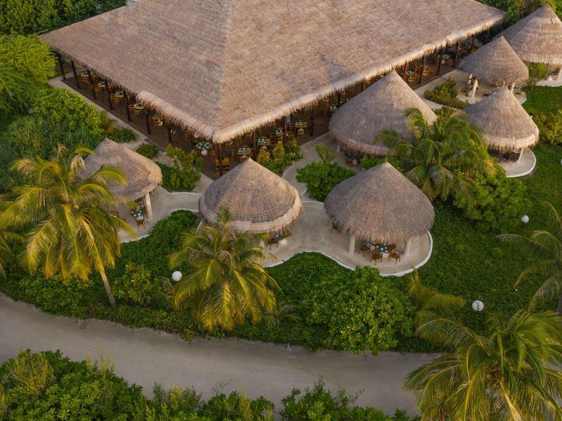 Villaggio con capanne rotonde con tetto di paglia e un grande edificio rettangolare circondato dal verde.