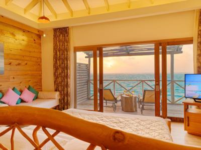 Chambre d'hôtel avec plafond en bois, lit confortable, canapé et vue sur la mer au coucher du soleil.
