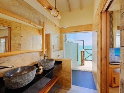 Salle de bain lumineuse avec lavabos en pierre, détails en bois et vue sur la mer par la porte ouverte.