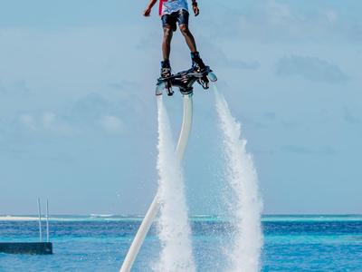 Person fliegt mit Flyboard über dem Meer vor klarem Himmel.
