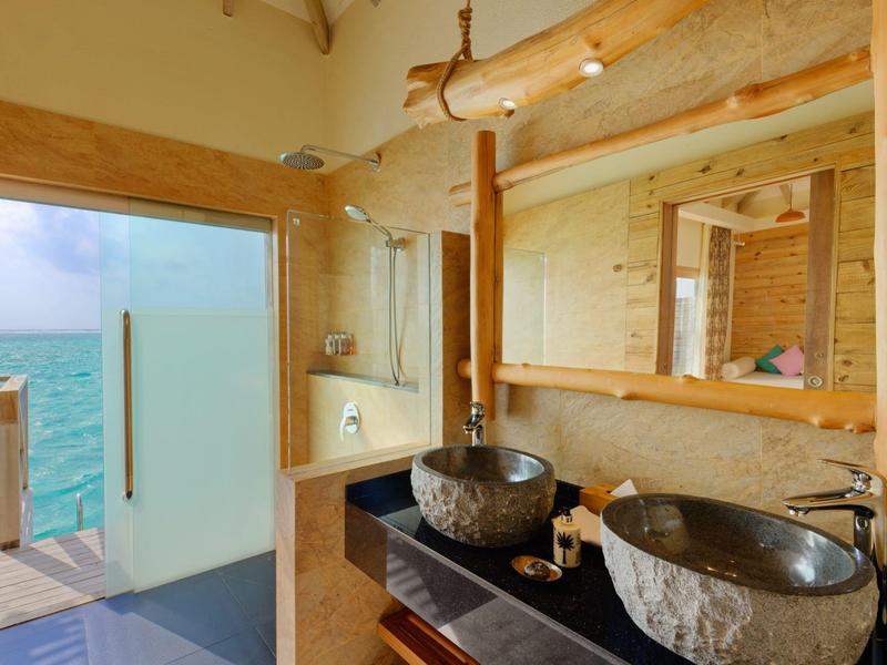Salle de bain moderne avec accents en bois rustique et vue sur la mer par la porte ouverte.