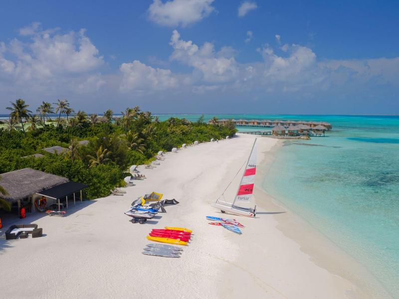 Plage de sable blanc avec chaises longues colorées et palmiers près d'une eau turquoise claire.