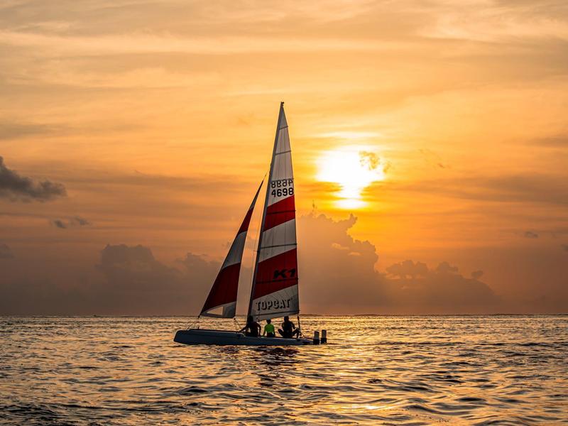 Voilier avec voiles rouges et blanches au coucher du soleil sur une mer calme.