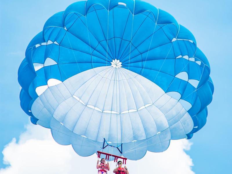 Deux personnes font du parachute ascensionnel avec un parachute bleu et blanc sous un ciel partiellement nuageux.