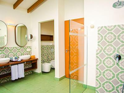 Salle de bain moderne avec carreaux verts, deux miroirs ovales et table en bois avec lavabos.