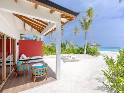 Véranda avec deux chaises devant un bungalow sur une plage de sable sous un ciel bleu.