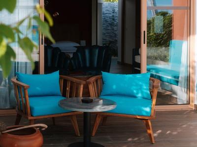 Terrasse confortable avec chaises en bois et coussins bleus devant une porte ouverte.