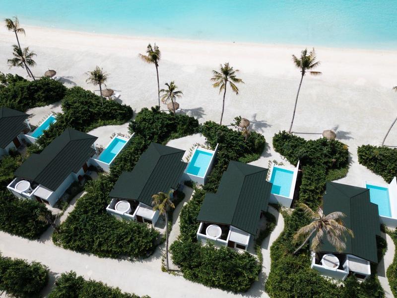Alignements de villas avec piscines privées sur plage de sable blanc et palmiers.