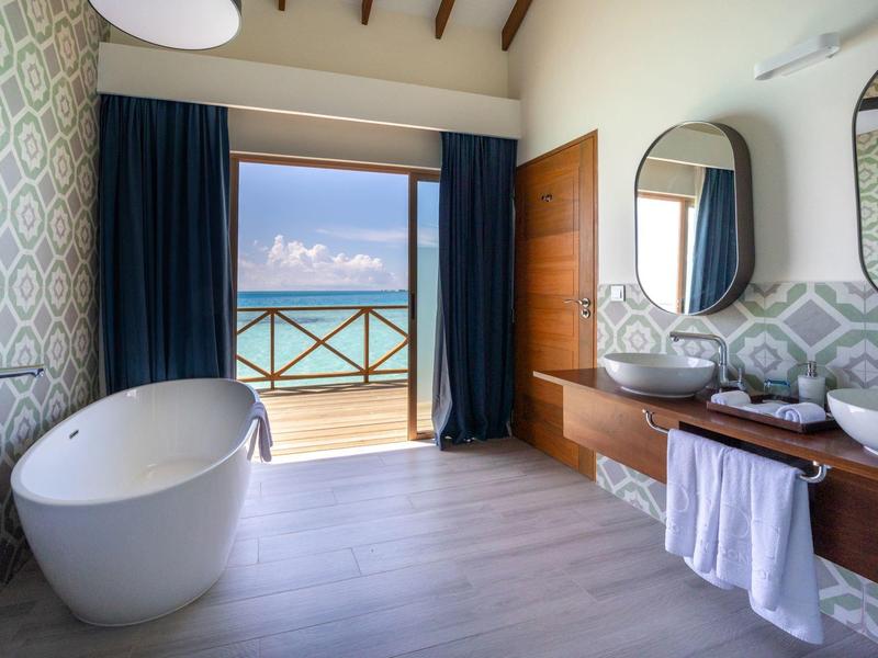 Salle de bain lumineuse avec baignoire indépendante, doubles vasques et vue sur la mer avec balcon.