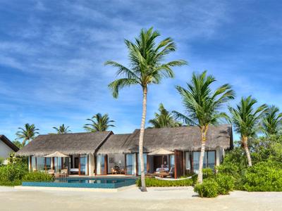 Resort sulla spiaggia con bungalow, piscina e palme sotto un cielo azzurro.