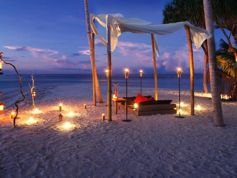 Ambientazione romantica sulla spiaggia con candele e baldacchino al tramonto
