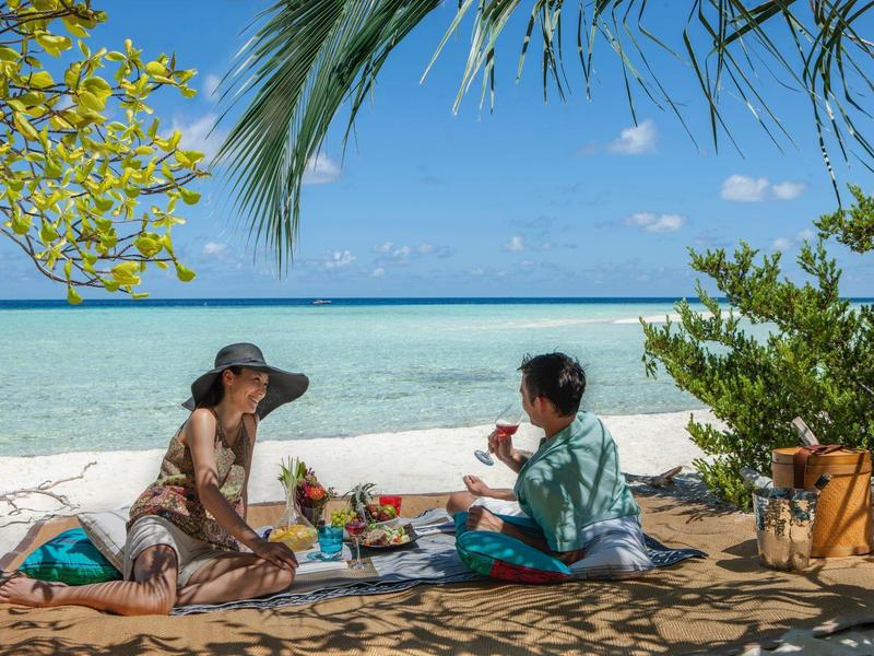 Due persone che godono di un picnic sulla spiaggia sotto le palme con vista sul mare.