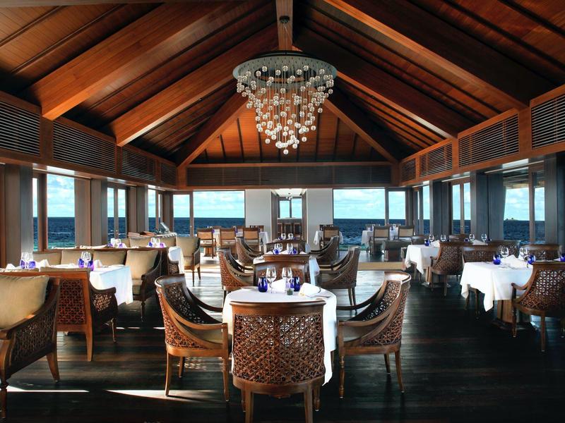 Ristorante elegante con tetto in legno, grandi finestre e aree salotto di design con vista sul mare.
