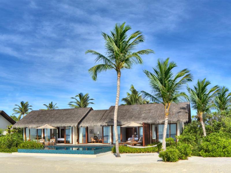 Villa sulla spiaggia con piscina, palme e cielo limpido vicino alla spiaggia sabbiosa.
