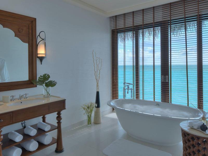 Bagno luminoso con vasca indipendente e vista sul mare attraverso grandi finestre con persiane.