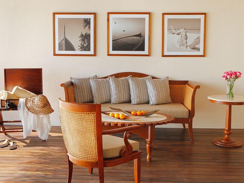 Soggiorno elegante con divano in legno, poltrone, tavolini e tre foto in bianco e nero sulla parete.