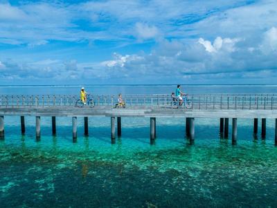 Ein Steg über klarem, blauem Wasser mit zwei Personen, eine joggt, die andere fährt Rad.