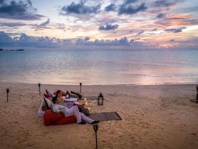 Ein Paar sitzt auf dem Sand am Strand, mit Blick auf das ruhige Meer bei Sonnenuntergang.