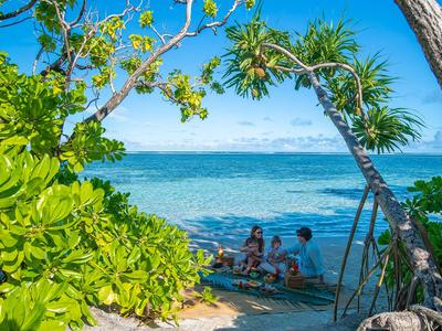 Gruppe von Menschen am Strand, umgeben von grünen Bäumen mit Blick auf das blaue Meer.
