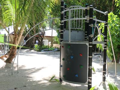 Klettergerüst aus Metall mit Kletterwand und Rutschstange im sonnigen Garten mit Palmen.