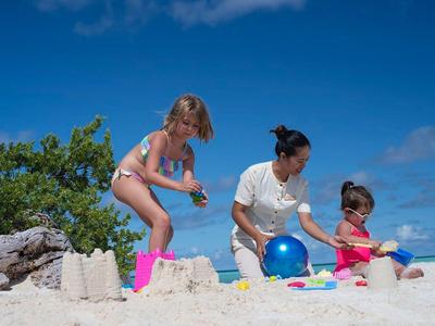 Drei Personen bauen Sandburgen am Strand bei klarem Himmel und blauem Ball.