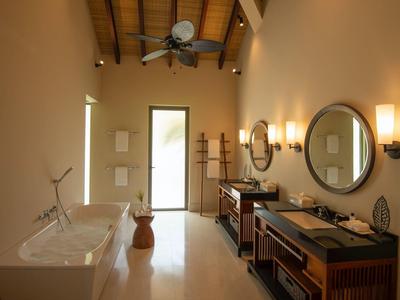 Geräumiges Badezimmer mit freistehender Badewanne, zwei Waschbecken, runden Spiegeln und Holzmöbeln.