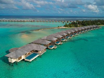 Reihe von Überwasser-Bungalows mit Pools vor tropischer Küste in klarem türkisfarbenem Wasser.